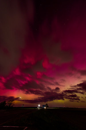 Vibrant red and purple aurora borealis over a rural landscape at night.の写真素材