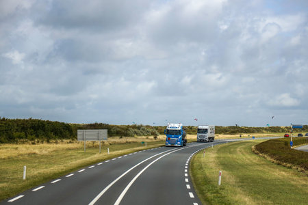 Two trucks driving on a rural highway under a cloudy sky.