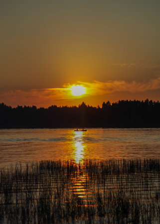A serene sunset over a lake, with silhouettes of trees in the background and a small boat on the waterの写真素材