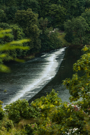 A serene river with a small waterfall surrounded by lush greenery.の写真素材