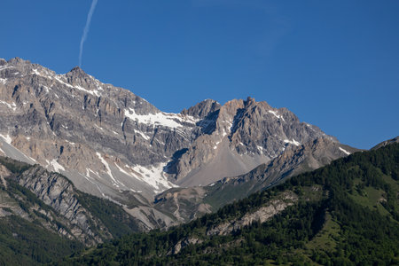Majestic mountain range with snow-capped peaks and lush green forest.