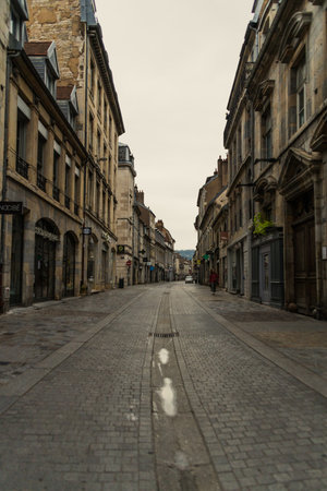 Empty cobblestone street lined with historic buildings under a cloudy sky.の写真素材