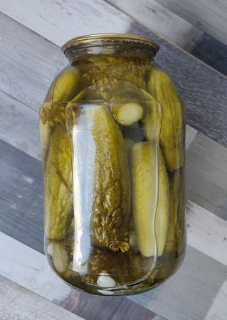 Pickled cucumbers in a glass jar. A jar of pickles lying on its side on the table. Preparing food...