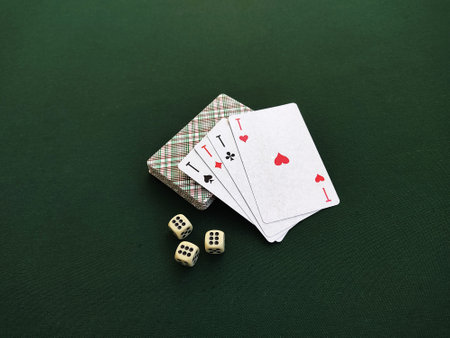 Four aces are on the deck of playing cards. Three dice with the name six are on the green table. Demonstration of gambling sports. Close-up photo.の写真素材