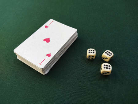 The ace of hearts lies on top of the deck of playing cards. Nearby are three bone dice with the name six on the green material of the game table. The concept of luck and demonstration of gambling, sports games.の写真素材