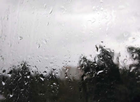 Raindrops run down the wet window glass of the house. View from the apartment window to the...