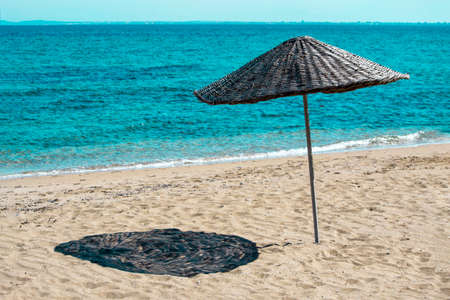 Braided straw umbrella on sandy beach near the green sea waterの写真素材