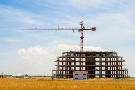 High construction crane and unfinished building. Mountains and blue sky on backgroundの写真素材