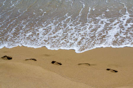 Footprints on the sand and the sea wave with foamの写真素材