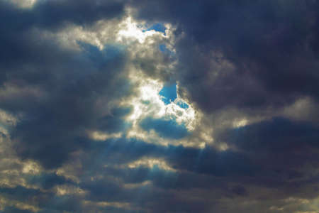 Sunrays going through dark heavy clouds. Piece of blue skyの写真素材