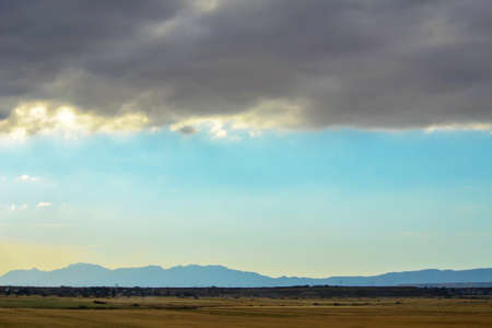 Dark heavy clouds high over blue sky, field and mountains. Layers of natureの写真素材