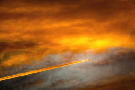 Inversion trail of the plane in the evening sky. The cloud, illuminated from below by the evening sun. Apocalypse aircraft.の写真素材