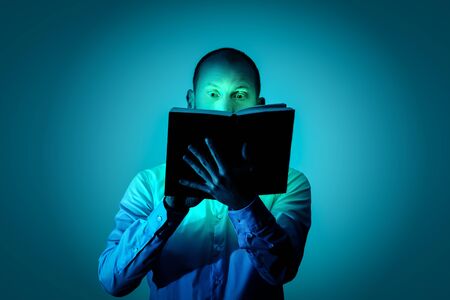 Man is fascinated by reading an exciting book and is illuminated by a magical lightの写真素材