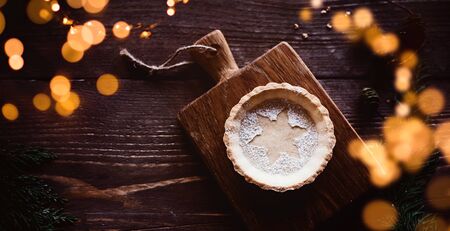 Traditional homemade Christmas pie on dark wooden background, with romantic lights and copy space / banner, header / flat lay, top viewの写真素材