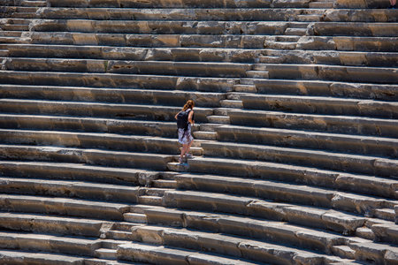 A young woman in a white dress stands on the steps of an ancient amphitheater