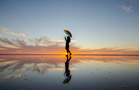 Silhouette of a woman with umbrella on the beach at sunsetの写真素材
