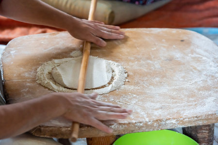 Close-up of female hands rolling dough with rolling pin on tableの写真素材