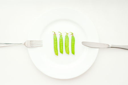 Four green peas in beans on the white plate with cutleryの写真素材