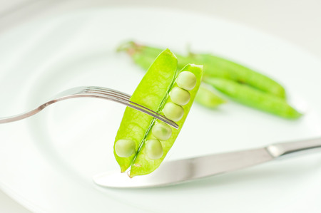Green peas on fork on the white plate with knifeの写真素材