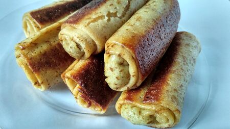 Appetizing pancakes rolled into rolls lie on a transparent plate on a white backgroundの写真素材