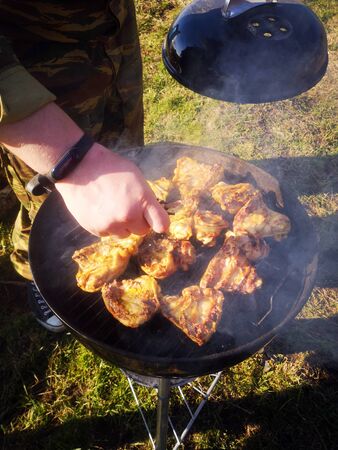 The male hand season the meat lying on the grill, with the other hand holds the lid of the grill, smoke is comingの写真素材
