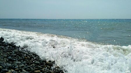 Sea wave rolls onto a large-pebble beach on a warm summer dayの写真素材