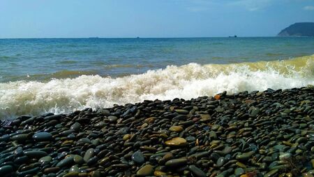 Sea wave rolls onto a large-pebble beach on a warm summer dayの写真素材