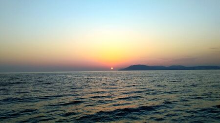 Sunset over the beautiful blue sea with mountain viewsの写真素材