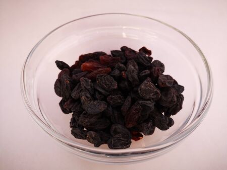 Appetizing raisins lies in a transparent plate on a white backgroundの写真素材