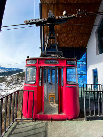 A red cable car parked at a mountain station with a snowy landscape and wooden roof in the background.の写真素材