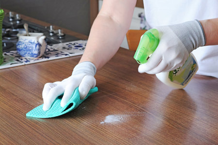 Woman in apron and gloves wipes down kitchen table with cleanser. House cleaning. . High quality...