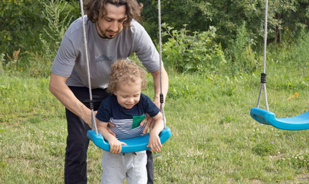 Dad train little boy to swing on playground swing. Lifestyle of family. Children and activity. . High quality photoの写真素材