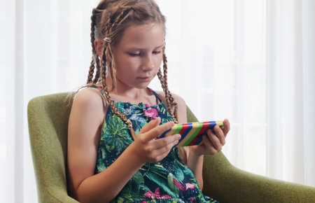 Teenage girl with lots of pigtails watches videos on her phone in room on chair. Technology and kids...