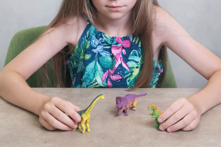 Teenage girl play with plastic dinasaurs on table at home. Toys and childhood. Animals and recreation. . High quality photoの写真素材