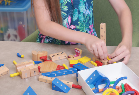 Girl assembles swing from magnetic wooden construction set. Toys and activiti children....