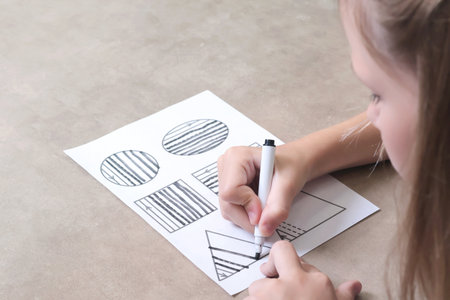 Schoolgirl draws lines with black pen. Writing practice. Childhood and activities at home. High...
