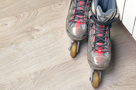Old roller skates with cloth shoe and plastic base near radiator on wood floor with rubber wheels....