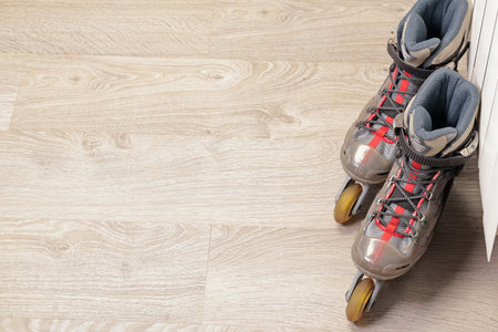 Old roller skates with cloth shoe and plastic base near radiator on wood floor with rubber wheels....