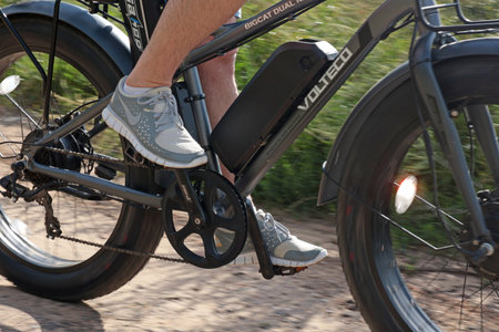Cyclist on electric bicycle riding along path in field in countryside at sunset close-up. Sport and...