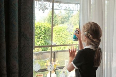Schoolgirl paint artificial frosting with snowflake stencil on window for Christmas. Decor and holiday. . High quality photoの写真素材