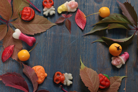 Frame of fall leaves, candy for Halloween. Holidays and food. Dessert in the shape of a pumpkin, skull, witch. Background for design. . High quality photoの写真素材