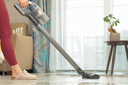 Modern upright cordless vacuum cleaner with dust light. Woman cleaning living room near sofa. . High quality photoの写真素材