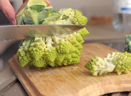 Anonymous cutting romanesco broccoli sprouts with knife on wooden board in kitchen. Healthy eating. Food and green vegetables. High quality photoの写真素材