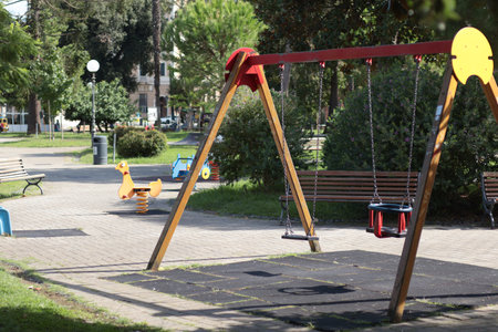 Playground with swings near trees in resort town in Italy. Park on sunny summer day. Lifestyle and...