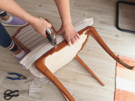 Anonymous person restore old vintage chair in home. Fabric replacement. Antique furniture and modern striped linen and cotton fabric. Hobbies, crafts, and retro-minimalist style. High quality photoの写真素材