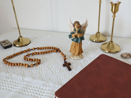 Catholic corner at home. Angel figurine, wooden rosary beads, cross, and prayer book. Faith,...