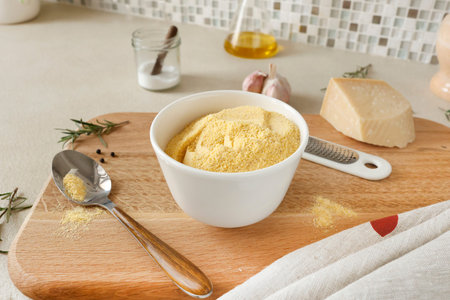 Corn flour in white ceramic bowl on wooden cutting board in kitchen. Parmesan and rosemary....