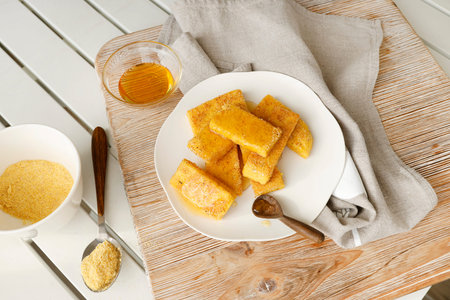 Slices of fried hard polenta with honey on plate on table. Cornmeal in kitchen. Ingredients and...