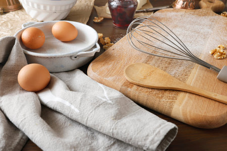 Baking preparation with brown eggs, whisk and wooden spoon on floured board. Close-up shot of rustic...