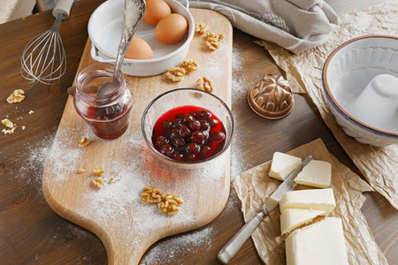 Baking ingredients with canned cherries, walnuts and fresh eggs on floured wooden board. High angle...